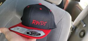 A Black flat brim hat with a red brim and trim. It also features the text RWDS on it, embroidered in red.