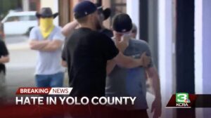 A screenshot of a newscast from KCRA 3. The Chiron reads, "Hate in Yolo County". One man, wearing a black shirt, holds back a man in a gray shirt. The man in the gray shirt is wiping his eyes with a napkin or tissue. 